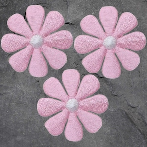 May include: Three embroidered pink daisy flower patches with white centers. The flowers are arranged in a triangular pattern against a dark gray, textured background. These patches are suitable for fabric crafts and embellishments.