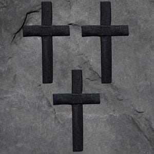 May include: Three black felt crosses on a gray stone background.