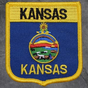 Peut inclure: Écusson brodé avec le mot "KANSAS" en noir sur une bannière jaune. Le patch a un fond bleu avec un emblème circulaire représentant un paysage. Le patch est bordé de coutures jaunes.