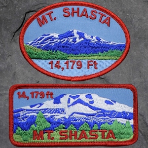 May include: Two embroidered patches depicting Mt. Shasta. One is oval, the other rectangular. Both feature a blue sky background with a mountain scene, green trees, and the text "MT. SHASTA" and "14,179 ft". The patches have red borders.