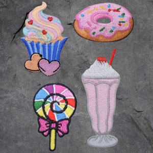 May include: Five embroidered iron-on patches featuring a pink and white cupcake, a pink and white doughnut, a pink and white milkshake, a rainbow lollipop, and a pink and white heart.