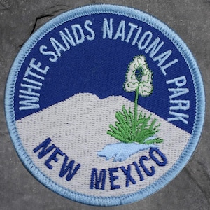 May include: Circular embroidered patch with the text "WHITE SANDS NATIONAL PARK" in white on a blue background. The patch depicts a desert plant and the words "NEW MEXICO" in blue.