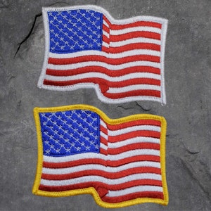 May include: Two embroidered patches of the American flag. The top patch has a white border, while the bottom patch has a yellow border. Both flags feature red and white stripes and a blue field with white stars.
