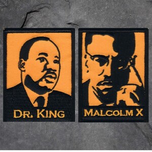 May include: Two embroidered patches featuring portraits of Dr. King and Malcolm X. The patches have a black border and background with orange centers. The text "DR. KING" and "MALCOLM X" are embroidered in gold thread.