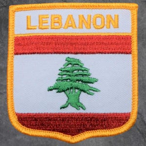 May include: Embroidered patch featuring the word "LEBANON" in gold lettering above a red stripe and a green cedar tree on a white background. The patch has a gold border.