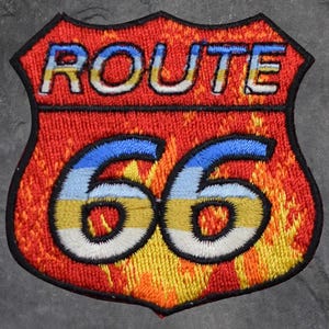 May include: Embroidered Route 66 patch in a shield shape. The patch features the word "ROUTE" in white letters with a blue and yellow gradient, and the number "66" in a similar style. The background is red with a flame-like design.