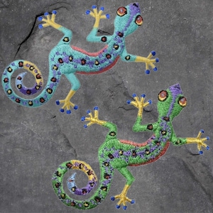 May include: Two embroidered green and blue geckos with yellow accents on a grey background. The geckos are facing opposite directions and have a detailed design.