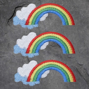 May include: Three embroidered rainbow patches with a white cloud and blue accents. The rainbow features red, orange, yellow, green, and blue arches. The patches are on a gray stone surface.