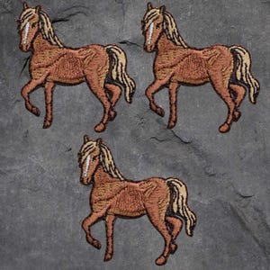 May include: Three embroidered patches of a brown horse with a tan mane and tail. The horse is depicted in a walking pose, with detailed stitching creating a textured appearance. The patches are arranged on a dark gray, textured surface.