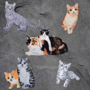 May include: Six embroidered cat patches in various colors and poses. The patches feature a gray cat, a calico cat, a gray tabby cat, a white cat with black markings, an orange tabby cat, and a gray and white tabby cat.