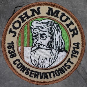 May include: Embroidered patch featuring a portrait of John Muir, with the text "JOHN MUIR CONSERVATIONIST" and the years "1838" and "1914". The patch has a tan background with brown and green accents.