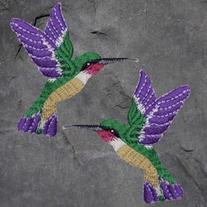 May include: Two embroidered hummingbird patches with purple wings, green bodies, and red throats. The hummingbirds are facing opposite directions.