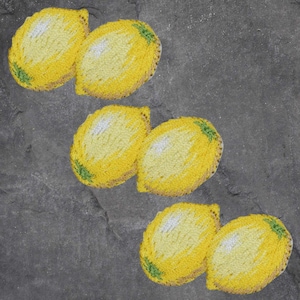 May include: Six yellow lemon-shaped coasters with green and brown accents are arranged on a gray surface. The coasters are made of a textured material, possibly yarn or fabric, and are designed to resemble lemons.