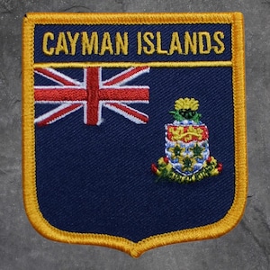 May include: A navy blue patch with a gold border featuring the text "CAYMAN ISLANDS" in gold lettering. The patch includes the Union Jack flag and the Cayman Islands coat of arms.