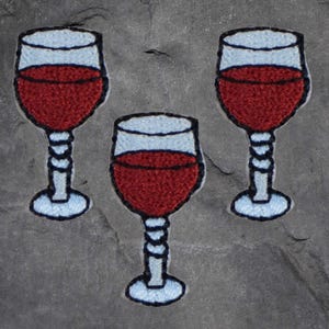 May include: Three embroidered patches of wine glasses filled with red wine. The glasses are white with a blue outline and the wine is a dark red.