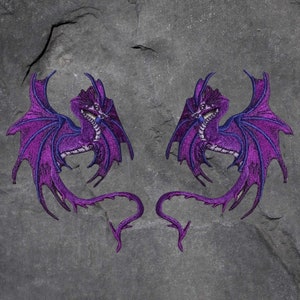 May include: Two purple embroidered iron-on patches of dragons with wings outstretched. The dragons have a detailed design with a scaly body and a long tail.