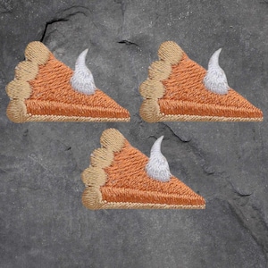 May include: Three embroidered pumpkin pie slices with a white swirl of whipped cream on top. The pie slices are a light brown colour with a tan crust.