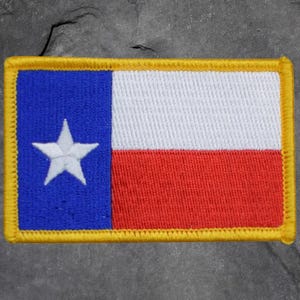 May include: Embroidered patch of the Texas state flag. The design includes a blue vertical stripe with a white star, a white horizontal stripe, and a red horizontal stripe. The border is yellow.
