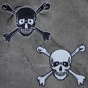 May include: Two embroidered patches featuring a skull and crossbones design. The top patch is black with white details, while the bottom patch is white with black details.