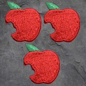 May include: Three red apple patches with a bite taken out of each, featuring green leaves. The patches are embroidered with a textured appearance. The apples are arranged on a dark grey, textured background.