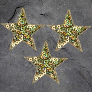 May include: Three gold star-shaped patches with iridescent sequins. The stars are sewn with gold thread.