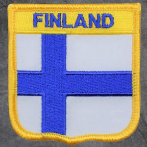 May include: Embroidered patch featuring the flag of Finland. The patch has a white background with a blue Nordic cross. The word "FINLAND" is embroidered in blue on a yellow banner at the top. The patch has a yellow border.