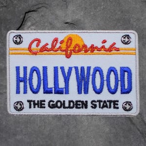 以下が含まれることがあります： カリフォルニアのナンバープレートに似た刺繍パッチ。「California」の文字が赤い筆記体で、「HOLLYWOOD」の文字が青いブロック体で書かれています。「THE GOLDEN STATE」の文字が下にあります。黄色の太陽のデザインが含まれています。