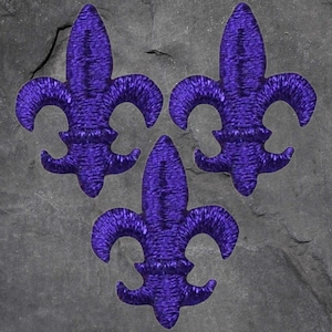 May include: Three embroidered purple fleur-de-lis patches arranged in a triangular pattern. The patches have a textured appearance and are set against a gray, textured background. The fleur-de-lis is a stylized lily.
