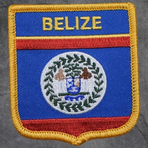 May include: An embroidered patch in blue, red, and gold, shaped like a shield. The word "BELIZE" is at the top. The central design is a white circle with a detailed emblem.