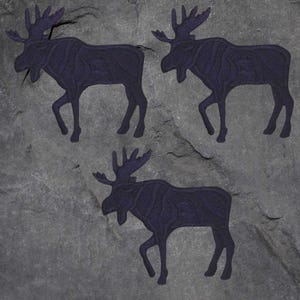 May include: Three dark blue moose silhouettes are depicted on a textured gray background. The moose are in a walking pose, with detailed antlers. The image has a rustic, outdoorsy feel, suitable for wall art or home decor.