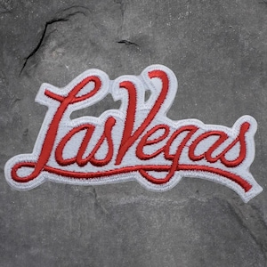 May include: Embroidered patch with the words "Las Vegas" in red cursive script, edged with white. The patch has a white border and is designed to be sewn or ironed onto clothing or other fabric items. Suitable for souvenirs or clothing.
