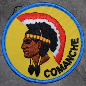May include: Embroidered patch featuring a profile of a Native American chief in a headdress. The patch is circular, with a yellow background, a blue border, and the word "COMANCHE" in bold letters.