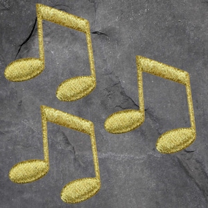 May include: Three gold-colored musical note patches with embroidered details. The notes are arranged on a dark gray, textured background. The patches are likely for sewing or crafting projects.