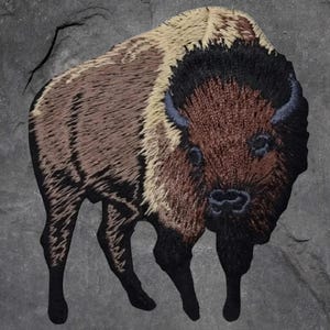 May include: Embroidered patch featuring a detailed bison design. The bison has a brown and black body with a tan mane and dark horns. The patch is set against a gray, textured background.
