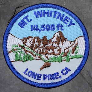 Peut inclure: Écusson brodé circulaire avec une bordure bleue. Il présente le texte "MT. WHITNEY" et "14,508 ft" au-dessus d'une illustration de montagne. Le texte "Lone Pine, CA" est en bas. L'écusson a un code couleur bleu clair, blanc, marron et vert.