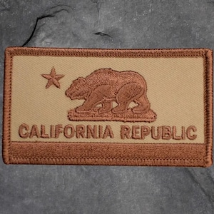 May include: A rectangular patch featuring the California Republic flag design. The patch has a tan background with a brown bear and star emblem. The words "CALIFORNIA REPUBLIC" are embroidered in brown below the bear.