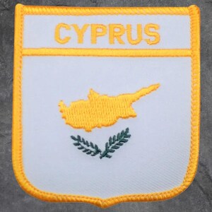 May include: A white patch with a yellow border and the word "CYPRUS" embroidered in yellow. The patch features a yellow outline of Cyprus and two green olive branches.