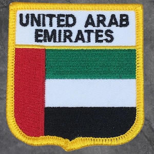 以下が含まれることがあります： アラブ首長国連邦の国旗が刺繍されたパッチ。パッチは白い背景に黒い文字で「UNITED ARAB EMIRATES」と書かれています。国旗のデザインには、赤、緑、白、黒のストライプがあり、黄色の縁取りが施されています。