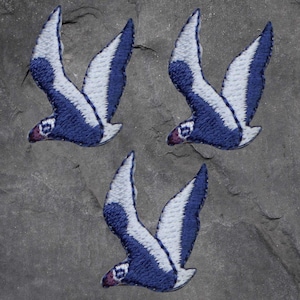 May include: Three blue and white embroidered bird patches. The birds are in flight with their wings spread out. The patches are perfect for adding a touch of whimsy to clothing, bags, or other crafts.