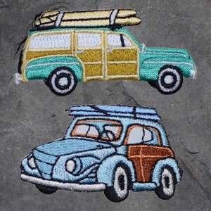 May include: Two embroidered patches of vintage station wagons. The top patch is a teal green station wagon with wood paneling and surfboards on the roof. The bottom patch is a light blue station wagon with wood paneling.