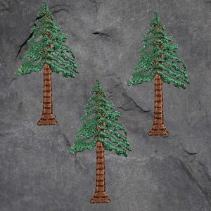 May include: Three embroidered evergreen tree patches. Each patch features a detailed green tree with brown trunk and base. The patches are arranged on a dark gray, textured background.