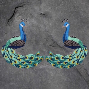 以下が含まれることがあります： 青、緑、黄色の刺繍が施された孔雀のアップリケが2つ。孔雀は反対方向を向いており、尾を広げています。
