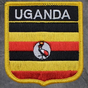May include: Embroidered patch featuring the flag of Uganda. The patch has a yellow border and displays the country's name in white letters. The flag design includes black, yellow, and red horizontal stripes, and a central emblem.