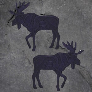 May include: Two black moose silhouettes carved into a gray stone surface.