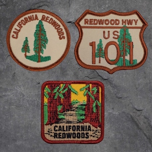 May include: Three embroidered patches featuring the text "California Redwoods" and "Redwood Hwy US 101". The patches are brown, beige, and red with green accents.