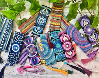 May include: A collection of hand-painted wooden bookmarks with intricate dot mandala designs. Each bookmark features a unique color palette, including blues, purples, and oranges, and is finished with a tassel. The bookmarks are approximately 6 inches long.