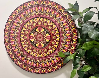 May include: A round, hand-painted mandala artwork. The design features a symmetrical pattern with shades of red, yellow, and brown on a black background. The artwork is a decorative piece, suitable for wall decor or as a focal point in a room.