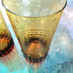 May include: Two amber glass tumblers with a textured, embossed design. The glasses have a dark amber base and a lighter amber top.