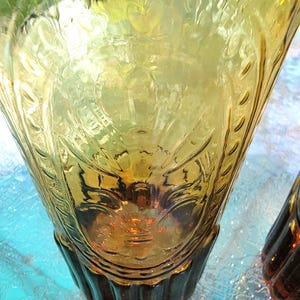 May include: Two amber glass vases with a textured, embossed design. The vases have a flared top and a ribbed base.