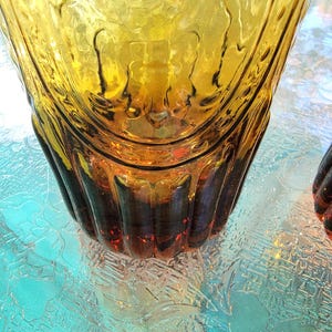 May include: A pair of amber glass tumblers with a textured, ribbed design. The glasses have a rounded bottom and a wide mouth.